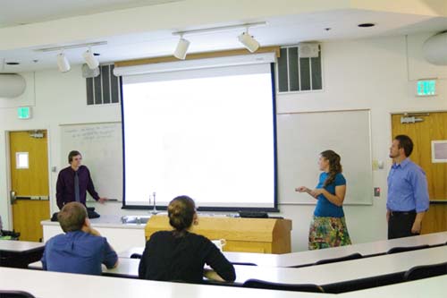Three students giving an oral presentation at the front of a classroom