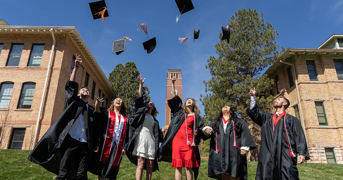 SUU graduates stand in a row and throw their caps in the air. 