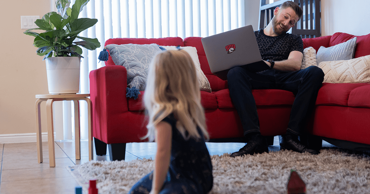 Dad smiles at his daughter while sitting on the couch with a laptop