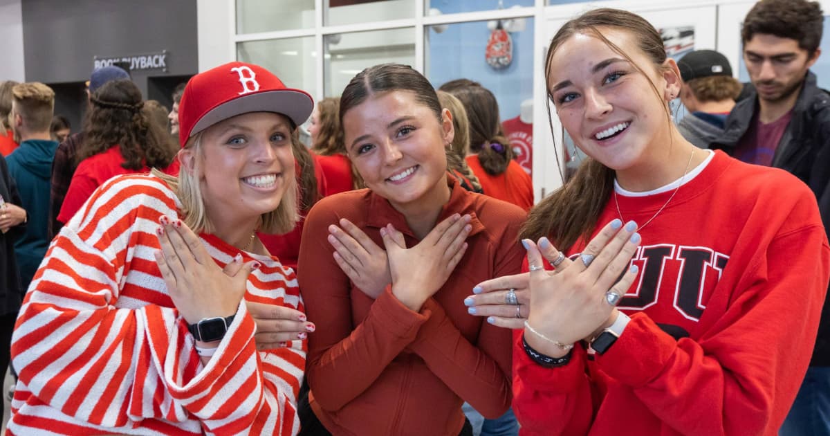 Three students wearing red and smiling at the camera while holding up the T-Bird hand sign.