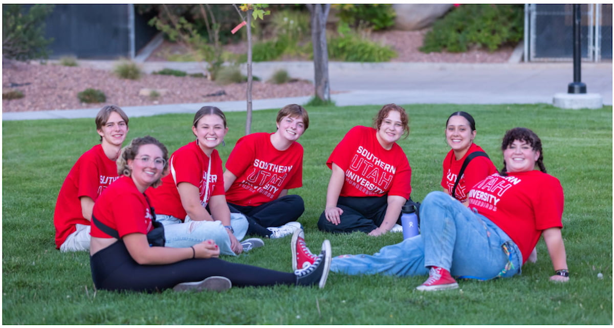 A group of students in red Thunder U shirts are sitting in the grass.