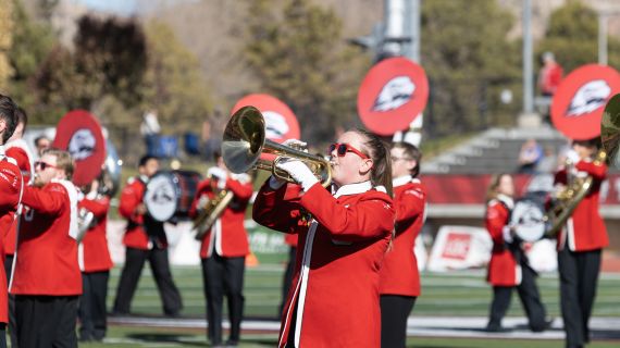 A performance of the Thunderbird Marching Band. A student is playing trumpet on a football field in formation with other students.